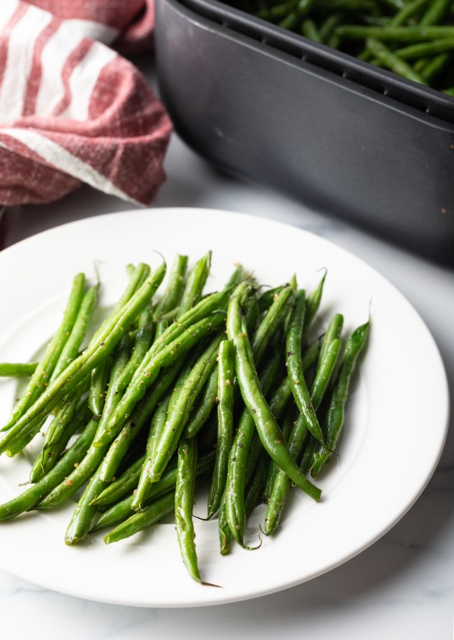 Pile of air fryer green beans on a white plate.