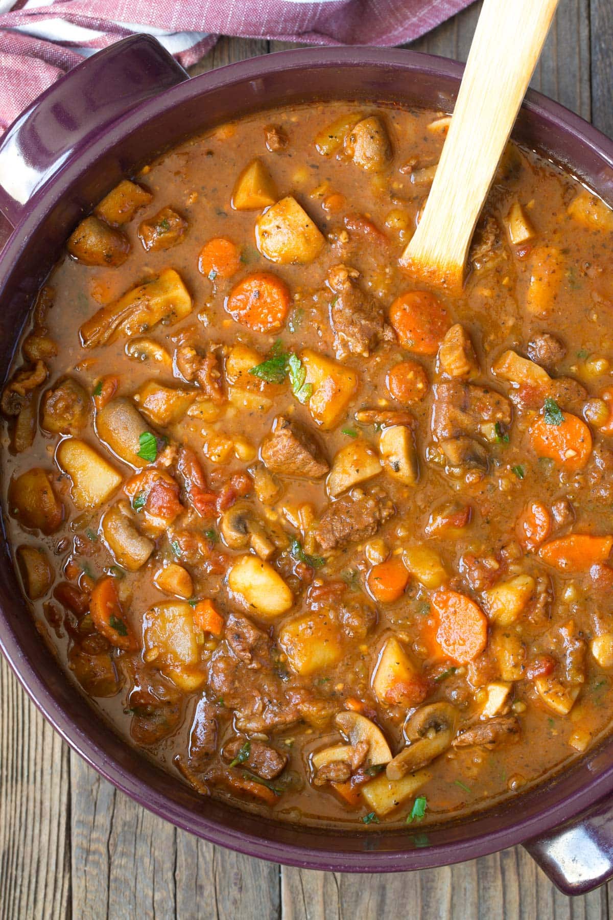 Beef Stew #ASpicyPerspective #BeefStew #BeefStewRecipe #Stew #StewRecipe #Beef #Crockpot #InstantPot #Stovetop #BeefStewCrockpot #SlowCookerBeefStew #BestBeefStew #HowtoMakeBeefStew Beef stew in dutch oven with a wooden spoon.