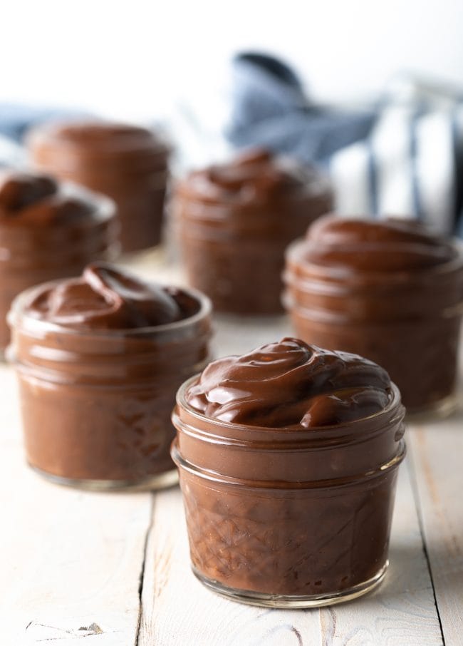 Small glass jars filled with homemade chocolate pudding on a wooden background.