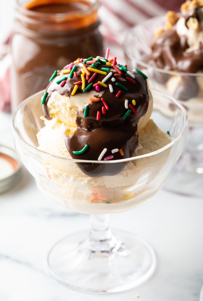 Glass dish with vanilla ice cream topped with the homemade fudge sauce and colorful sprinkles.