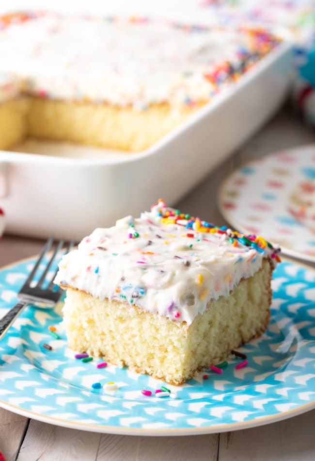 Slice of vanilla cake with funfetti frosting served on a blue plate.