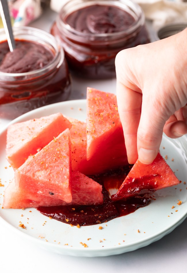 Hand dipping wedge of melon into thick chamoy sauce.
