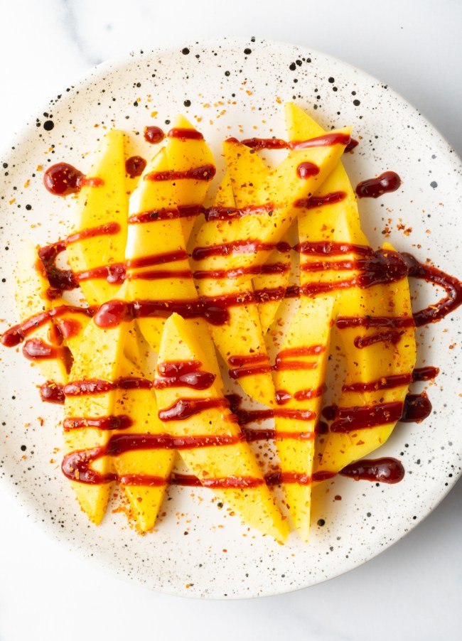 Top down view pieces of mango on a plate, drizzled with chamoy sauce.