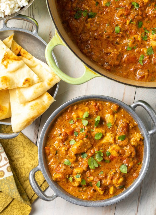 Easy Chicken Curry Recipe - Madras curry in a Dutch oven with more in a bowl next to some naan bread.