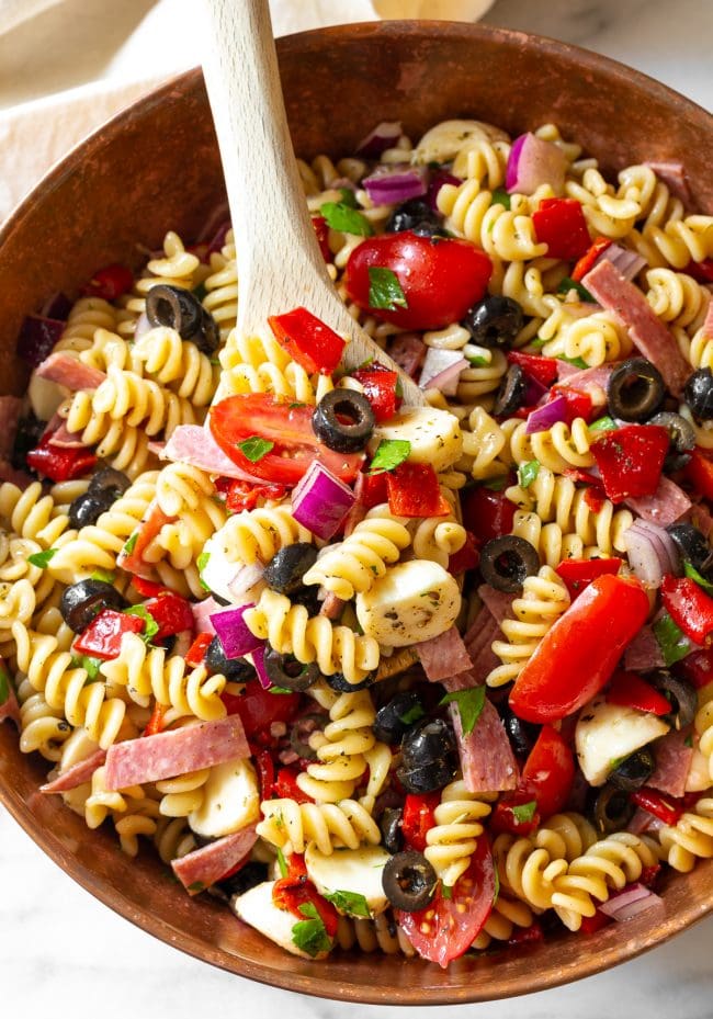 Pasta Salad #ASpicyPerspective #PastaSalad #PastaSaladRecipe #ItalianPastaSalad #Italian #Salad #BestPastaSalad #Spring #Summer Italian pasta salad in a bowl with a wooden spoon.