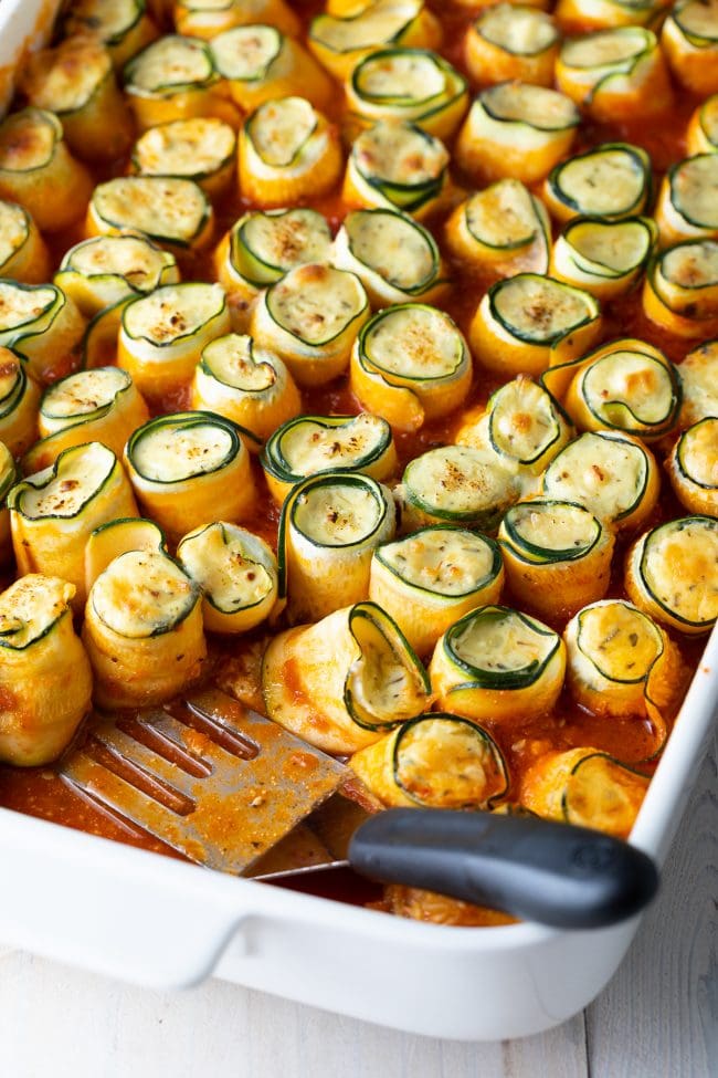 keto zucchini lasagna roll ups in a baking dish with a spatula in the dish.