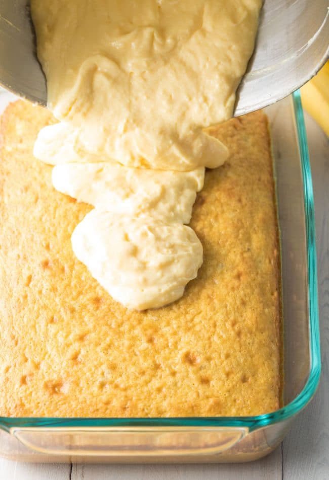 Creamy pudding layer going on top of the cake layer in a baking dish. 