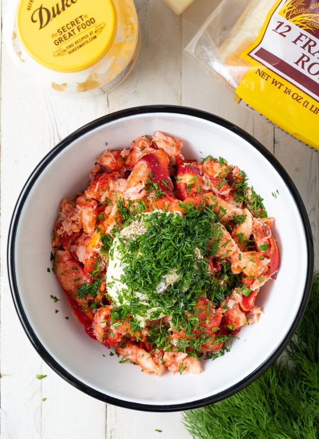Lobster in a mixing bowl with the dressing on top. 