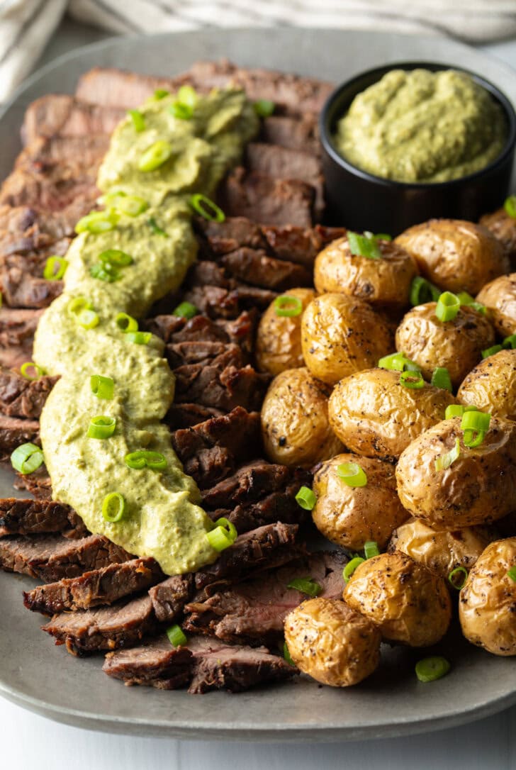 London broil sliced into thick strips, covered with rich green sauce and chopped scallions with baby potatoes on the side.