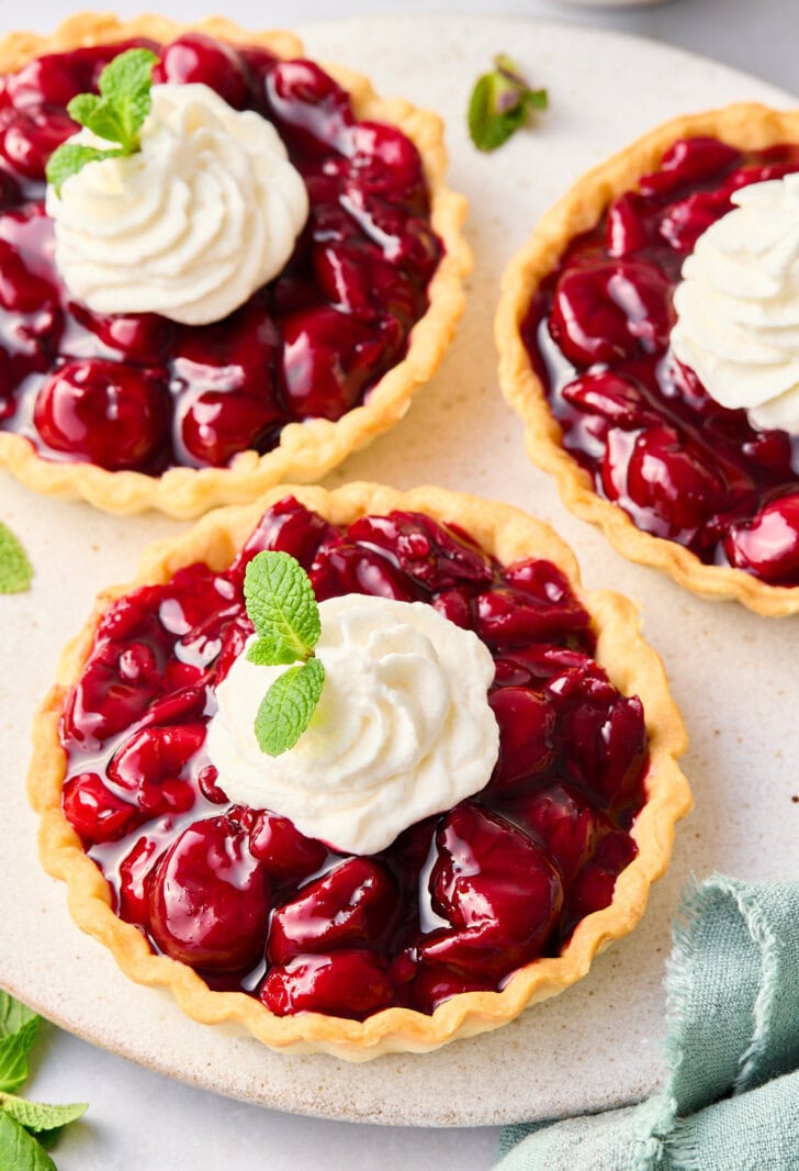 Three mini cherry tarts topped with whipped cream.