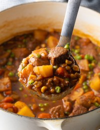 Ladleful of Mulligan stew with chopped potatoes, carrots, peas, and chunks of beef.
