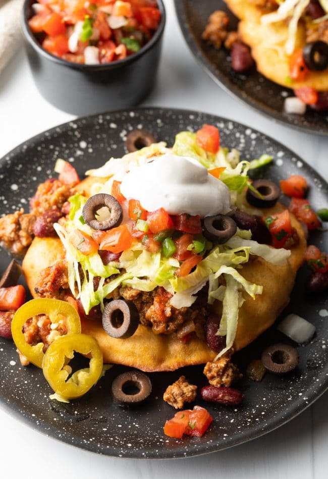 Navajo fry bread topped with ground beef and other taco toppings on a black plate.