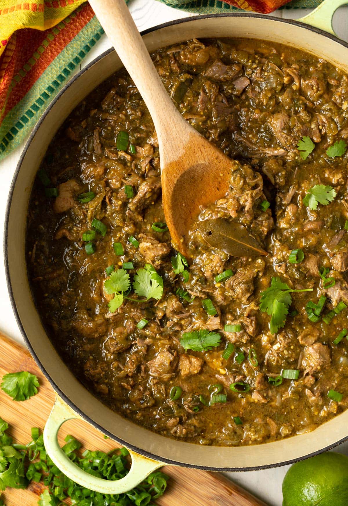 Dutch oven full of pork green chili with a wooden spoon.