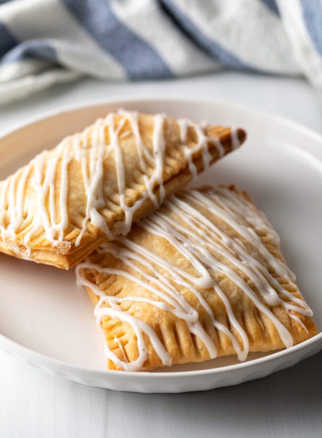 Two homemade peach pop tarts resting against each other on a white plate.