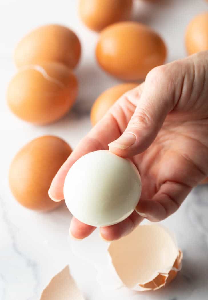 Hand holding a peeled egg to camera.