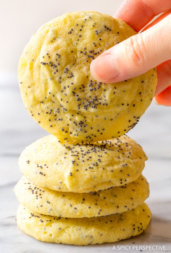 Lemon Poppy Seed Cookies #ASpicyPerspective #Lemon #PoppySeed #SoftCookies #EasyLemonCookies #PoppySeedRecipes #PoppySeedCookies #Summer #Spring #Easter Hand holding a lemon poppy seed cookie recipe with more cookies stacked underneath.