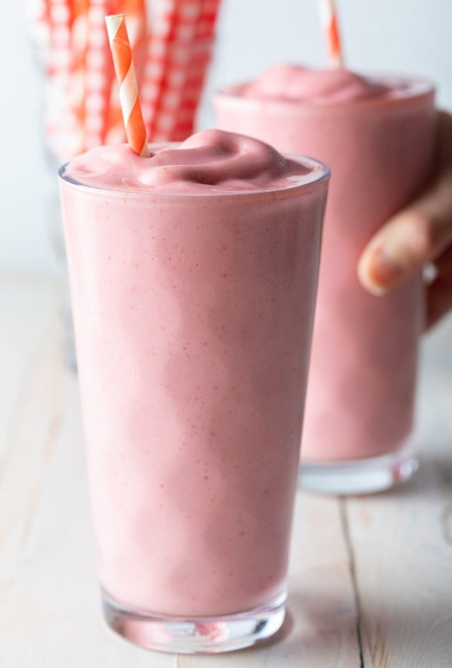 Strawberry Smoothie Recipe - Two strawberry smoothies with a hand grabbing one of the glasses. 