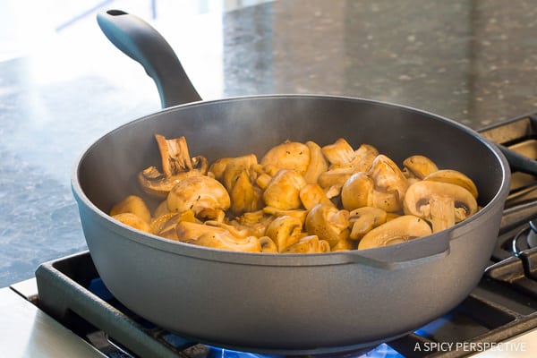 Mushrooms sautéing in a pan on the stove. 