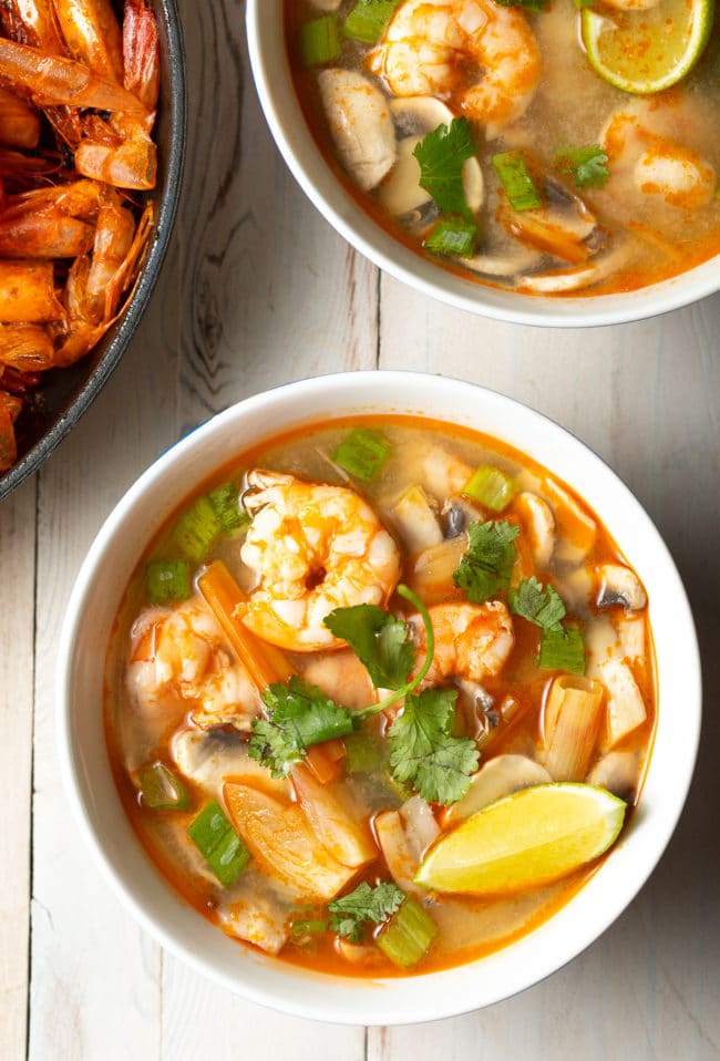 Overhead shot of bowl of tom yum with cilantro and lime wedges on top.
