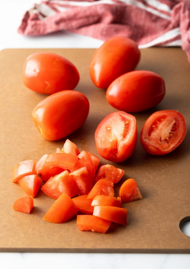 Tomatoes being chopped into pieces on a cutting board. 