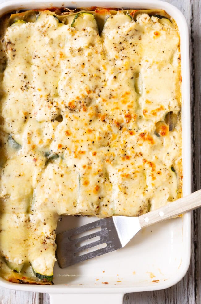White vegetable lasagna in a white baking dish with a few portions of lasagna missing.